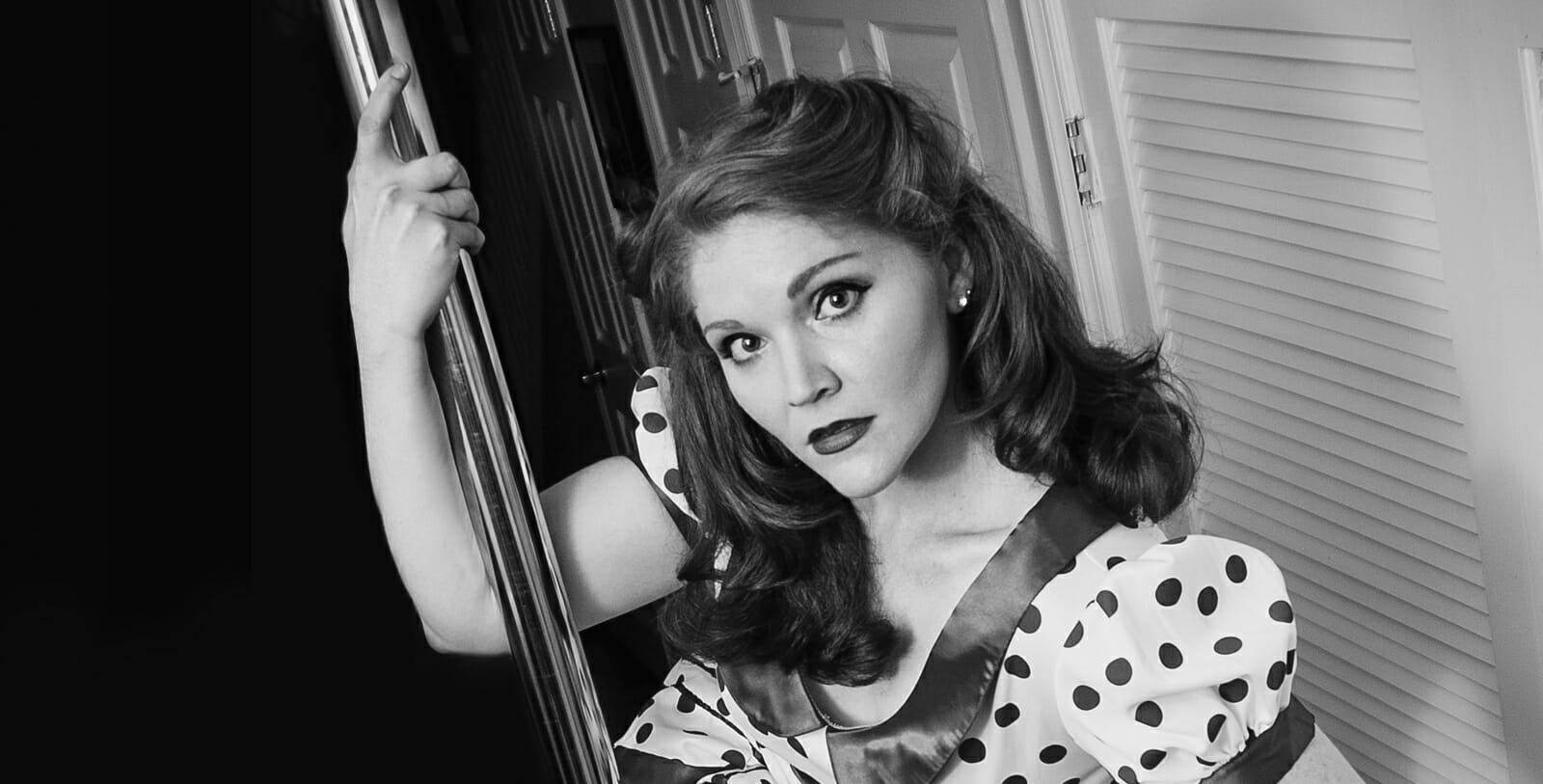 Black and white photo of Colleen Jolly dressed pin-up style holding a pole.