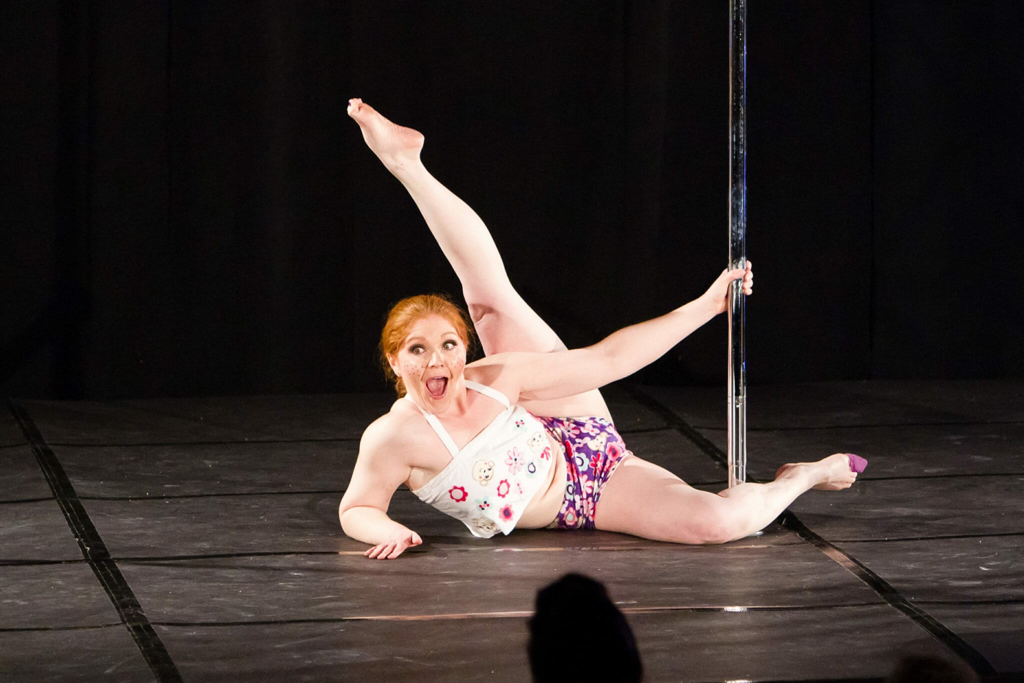 Colleen Jolly performing on stage doing pole floor work.