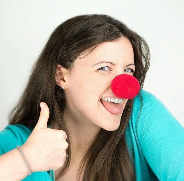 Smiling woman gives the camera a thumbs-up while wearing a clown-nose.