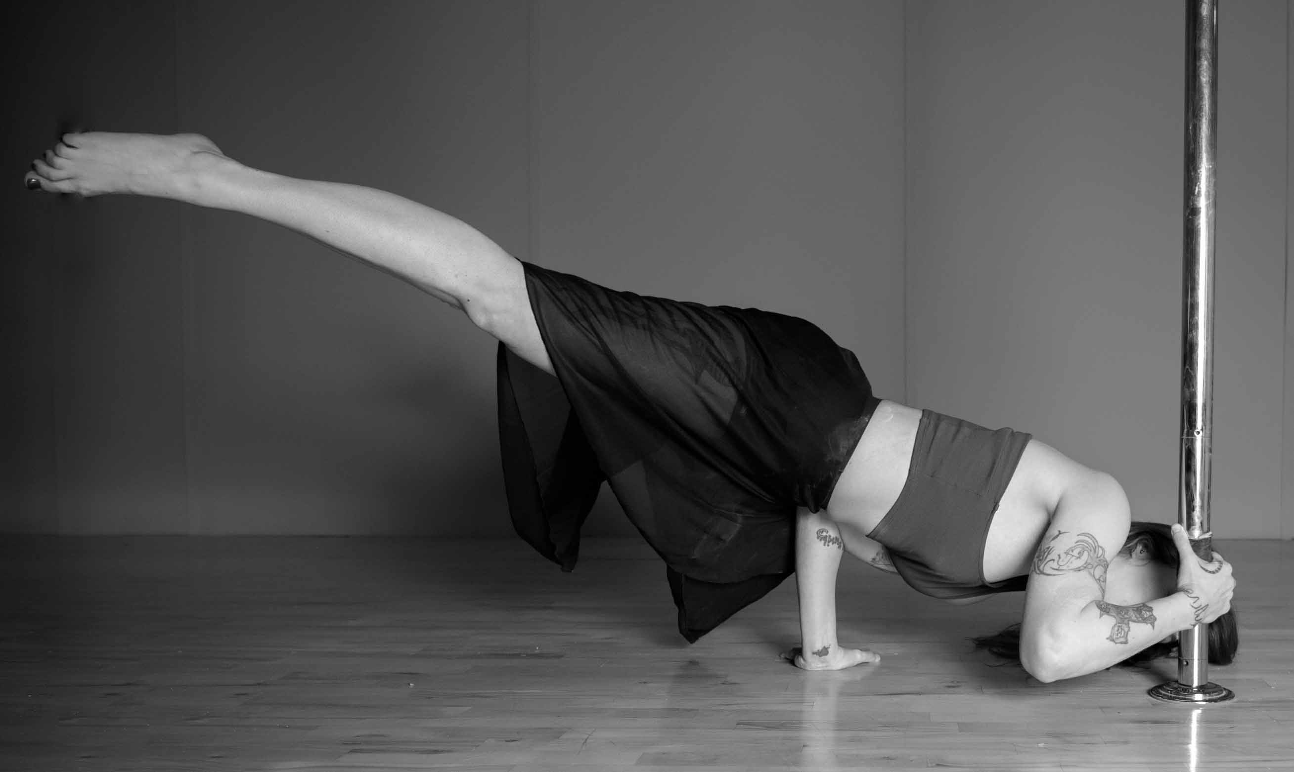 Pole dancer balances in plank/planche with one hand on the floor and another on the pole.