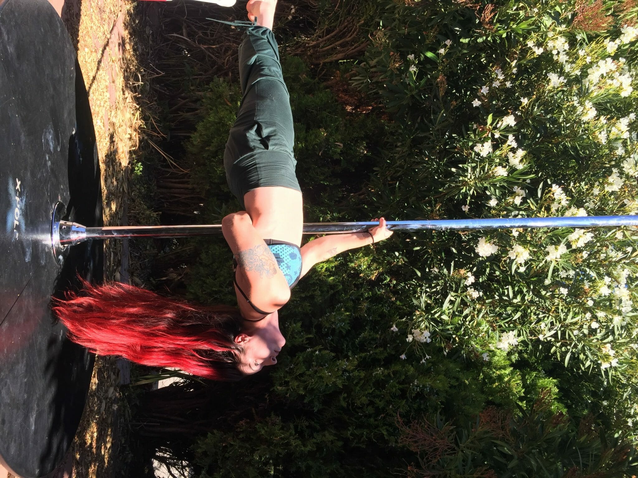 Pole dancer executes tabletop on an outdoor stage pole.