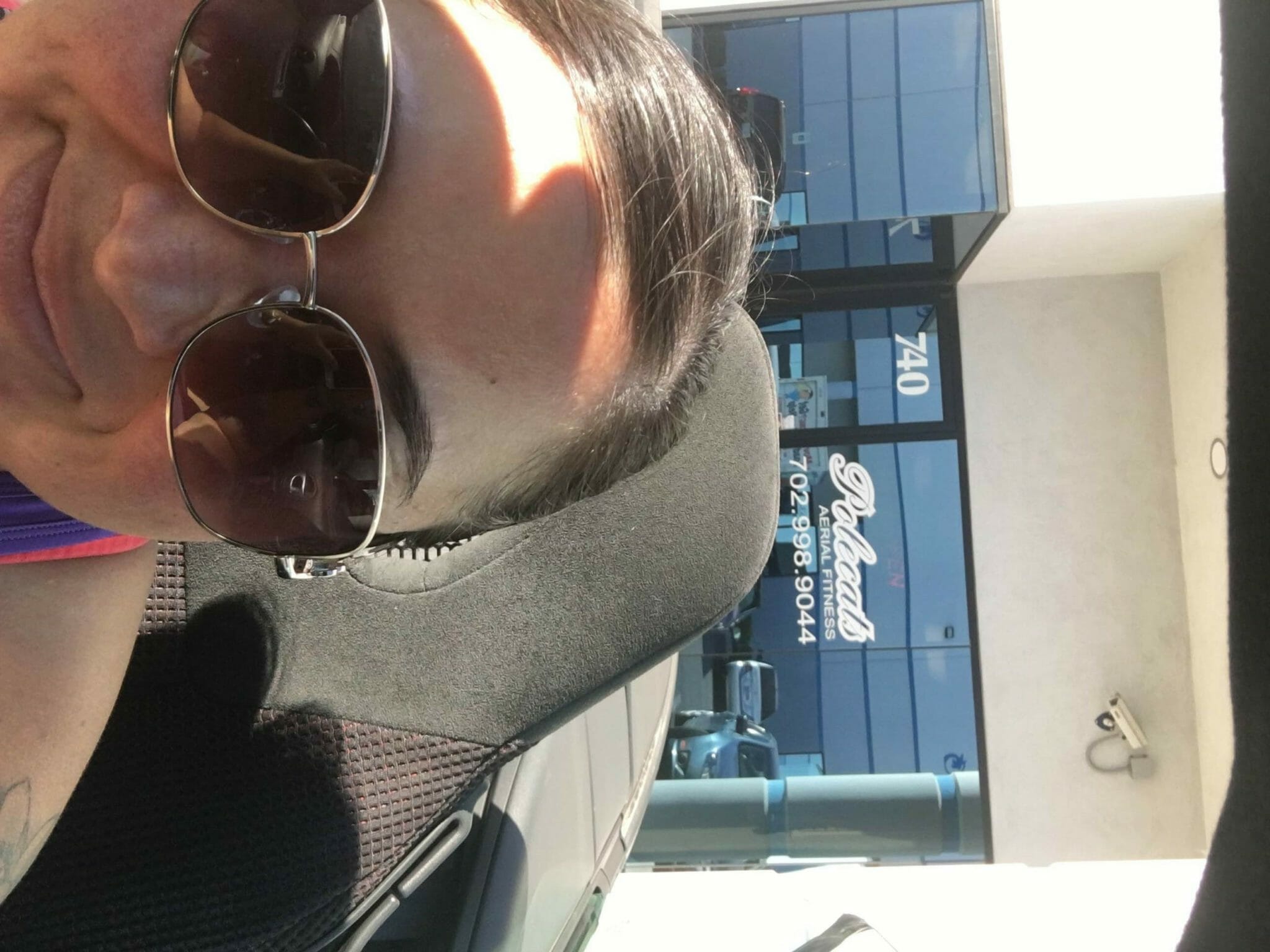 Individual takes a selfie with dark sunglasses and an aerial studio front door in the background.