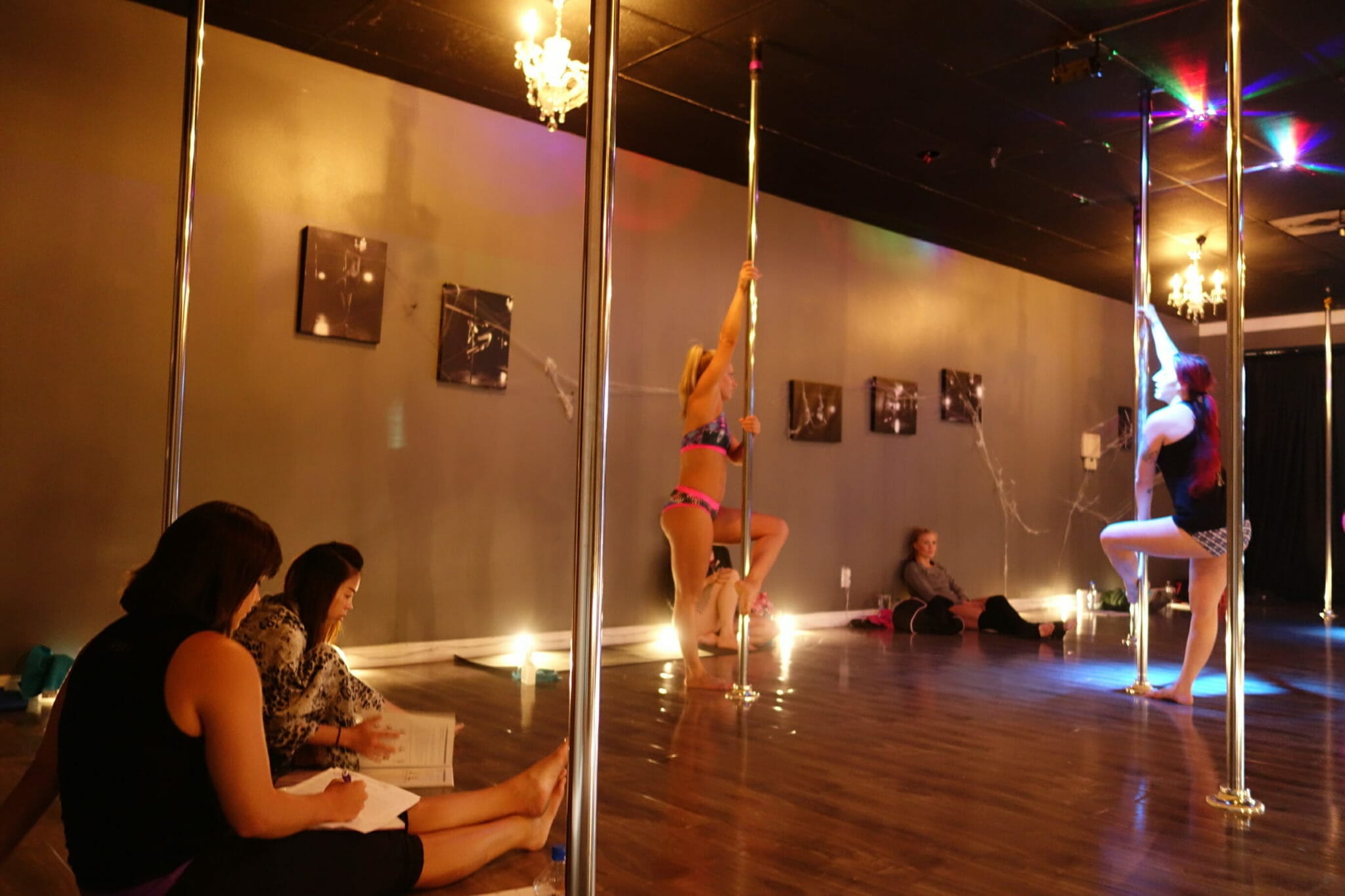 students practice on poles while others take notes along the studio edges