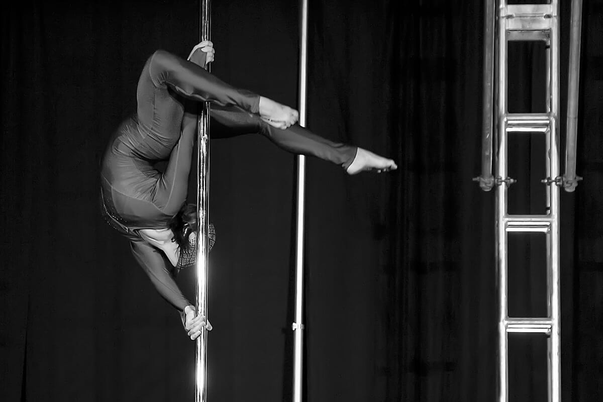 Pole dancer executes advanced inverted tricks wearing a full body suit.