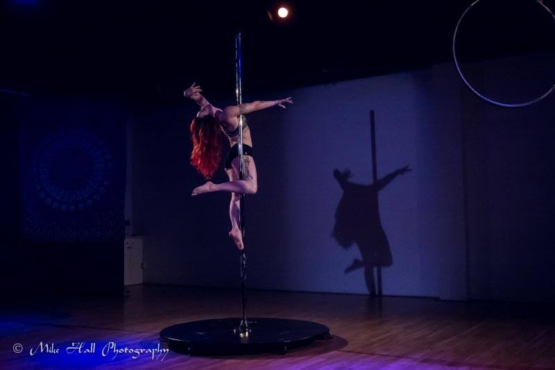 pole dancer on a stage pole with her silhouette highlighted on the wall