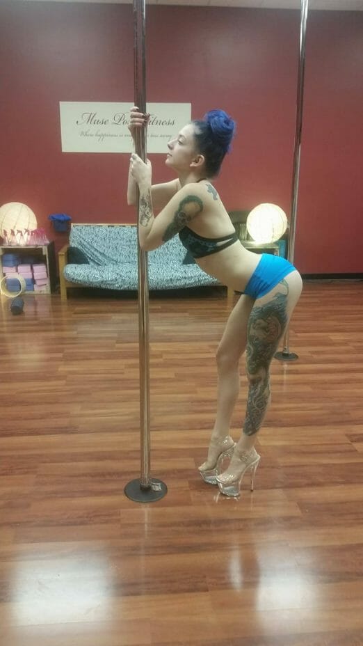 Pole dancer demonstrates a body wave in a studio.