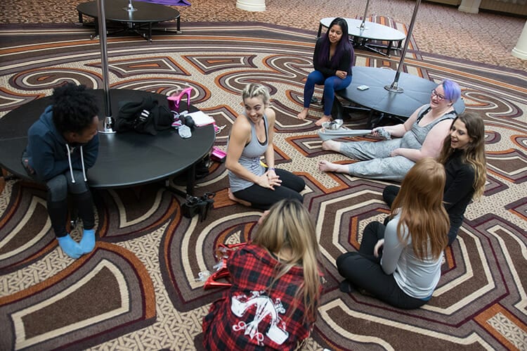 Students sit on the floor next to stage poles between workshops