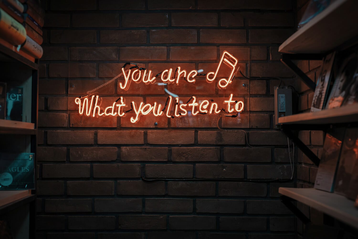 brick wall with neon sign: you are what you listen to