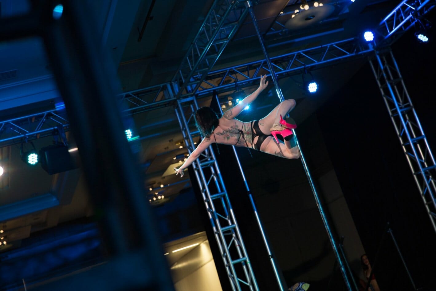 Back view of a pole dancer doing a knee hold on stage