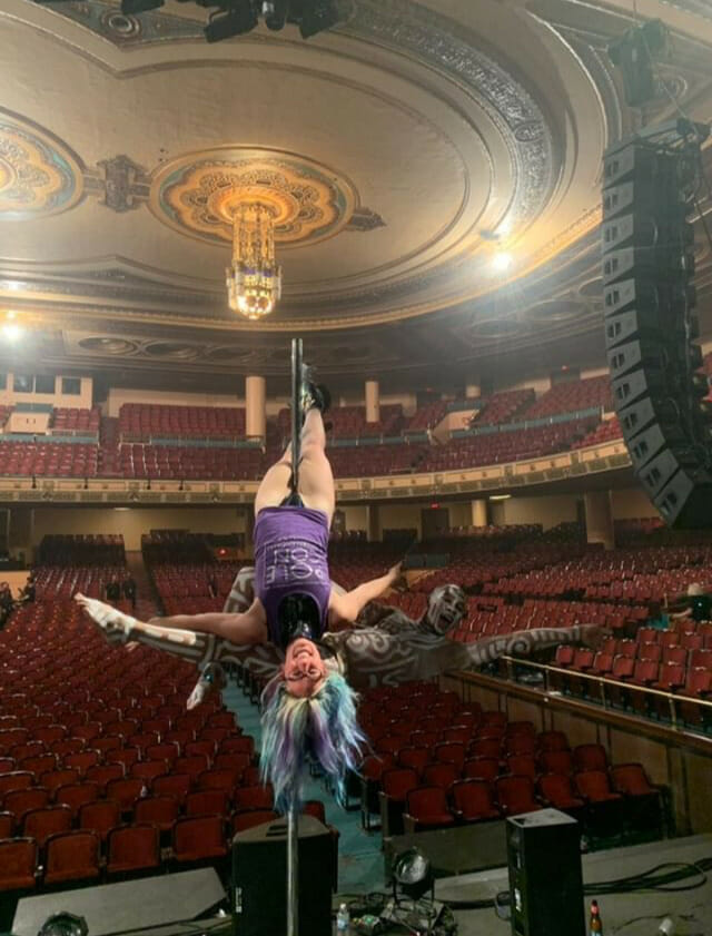 Doubles pole dancers pose in a large empty theater