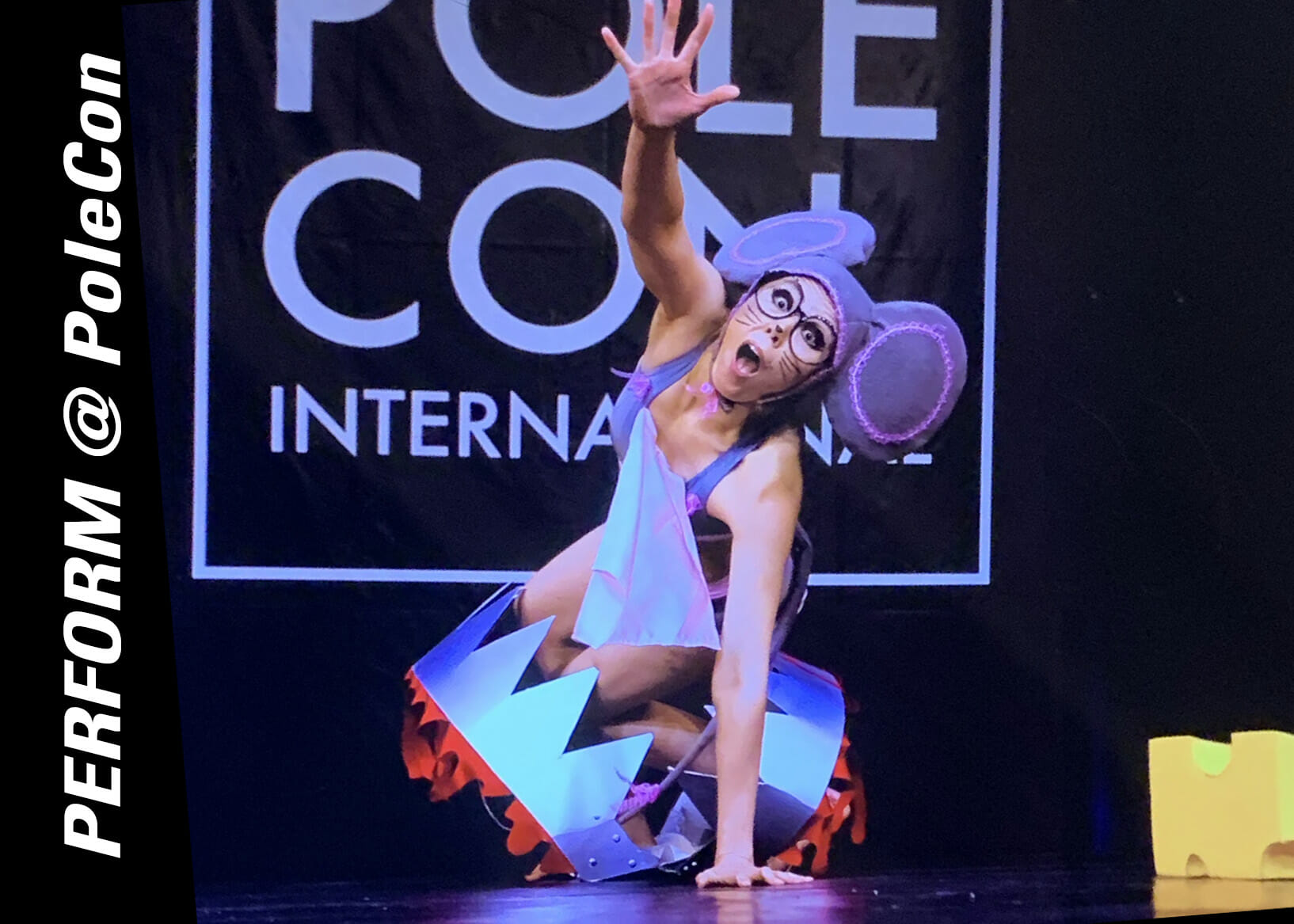 Performer in large mouse ears crawls out of an oversized trap on stage.