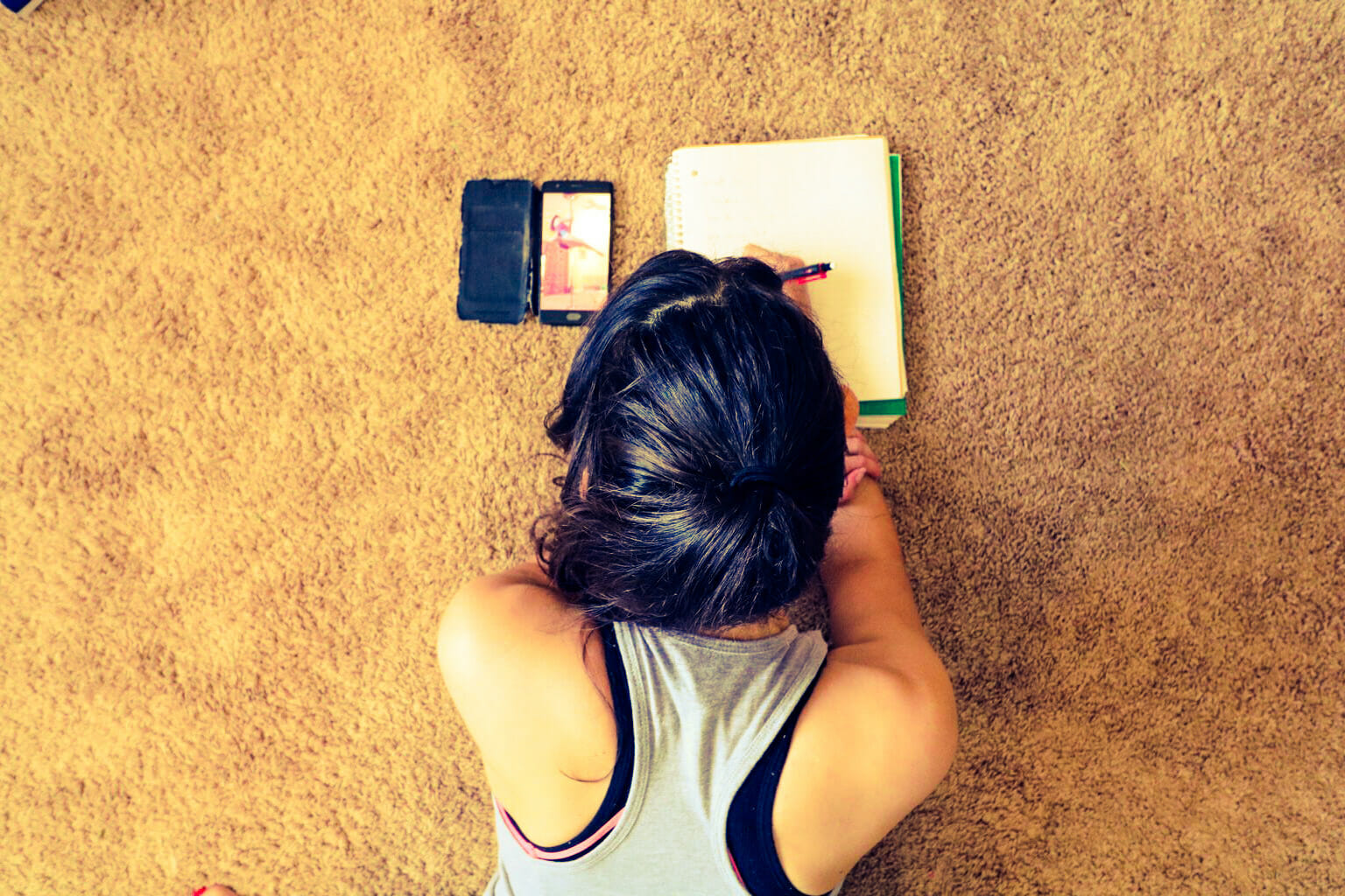 Student lays on the floor watching pole videos and taking notes