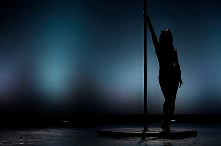 Dark silhouette of a dancer leaning on a pole with blurred background.