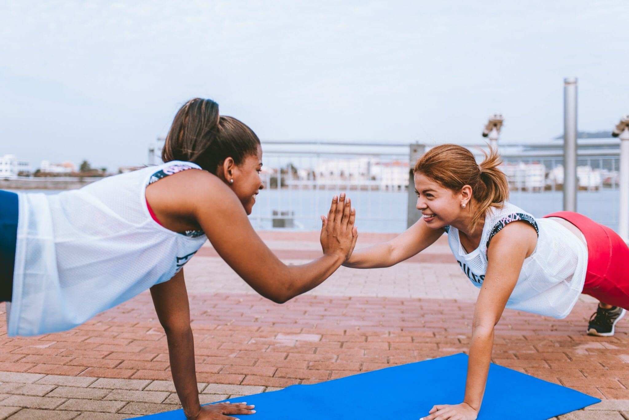 Two individuals high five each other from plan position in front of a dock setting.