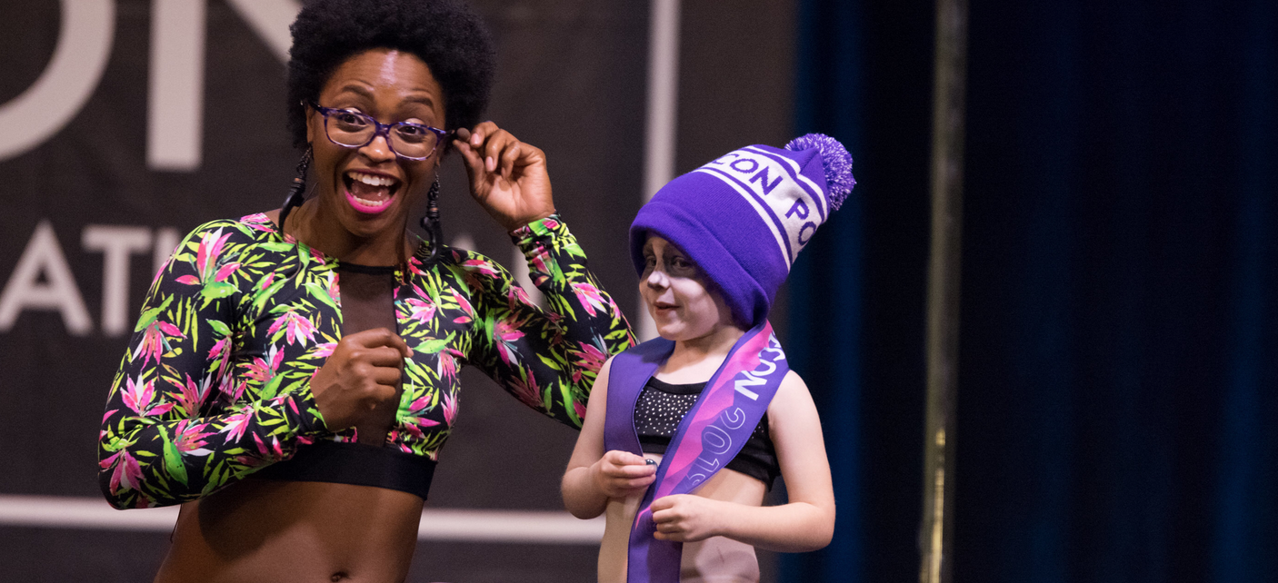 MC on the stage with a small person wearing a PoleCon hat.