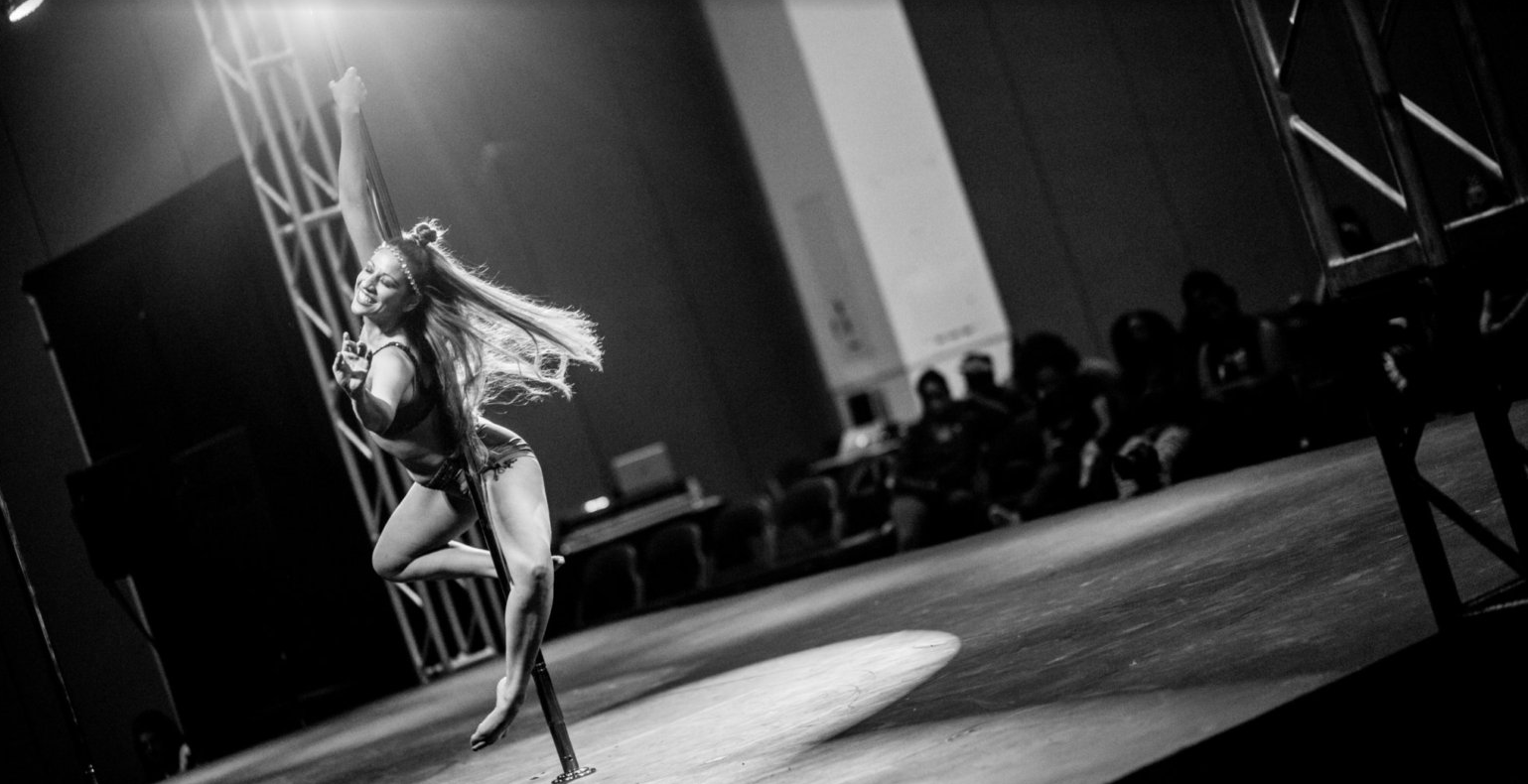 Dancer spins around the pole while wearing a huge grin