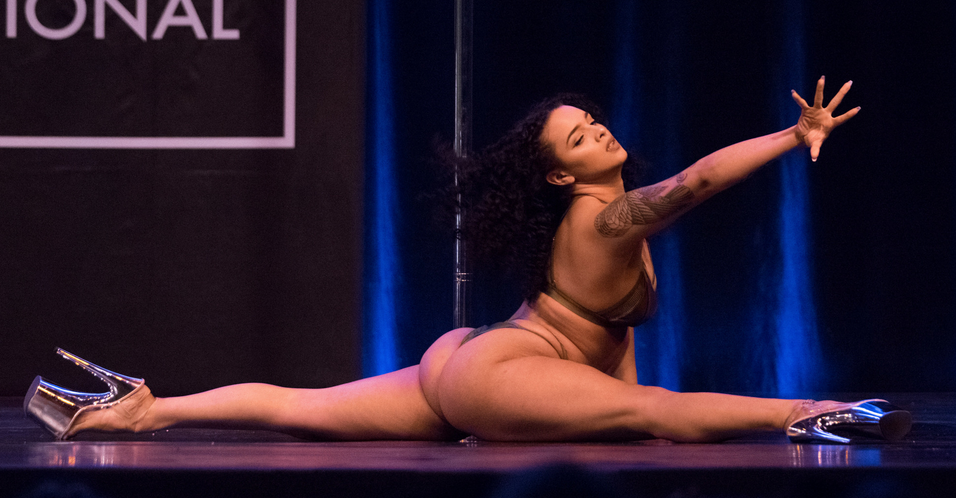 Dancer executes the floor splits on stage while reaching for something off camera.