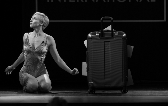 dancer on stage next to an over-stuffed suitcase.