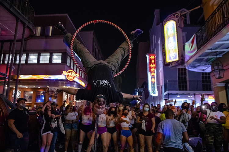 Male presenting street performer demonstrates on a lyra in front of a crowd.