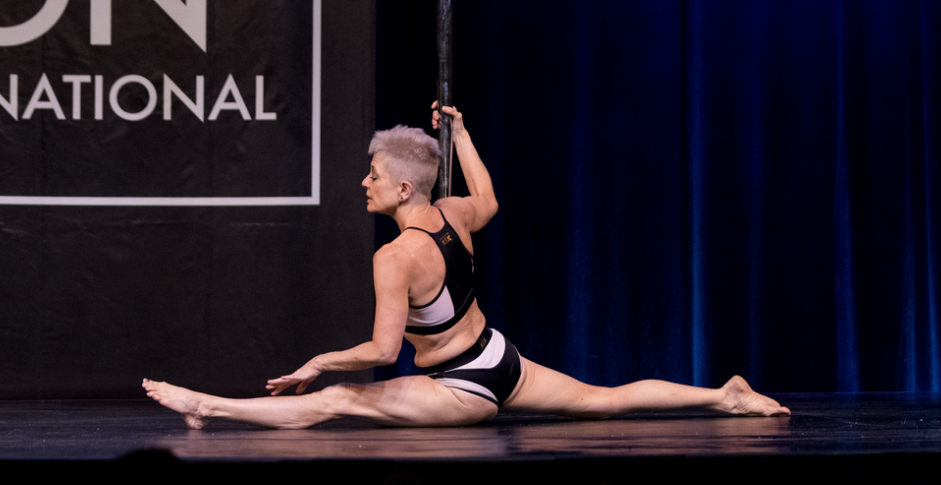 Pole dancer executes floor splits on stage.