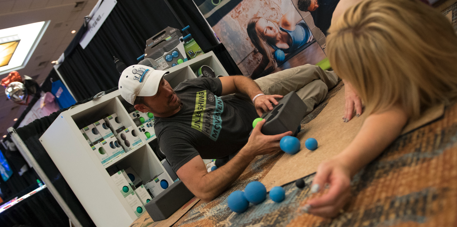 Vendor explains yoga ball and peanut to customer at a booth.