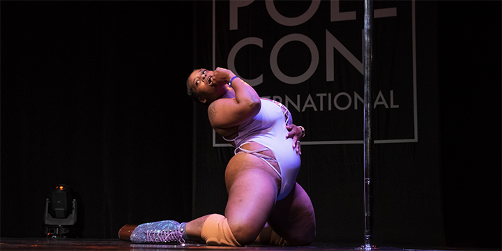 Dancer kneels in front the pole looking at the audience