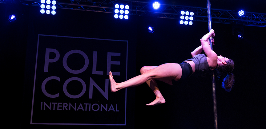 Pole dancer executes a shoulder mount while simulating air walking.