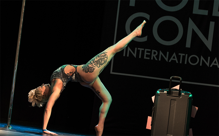 Pole dancer performs on stage with a suitcase center stage.