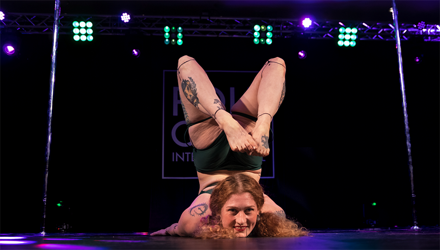 Pole dancer demonstrates flexibility with a floor chest-press and back-bend with toes nearly curled to the back of the head.