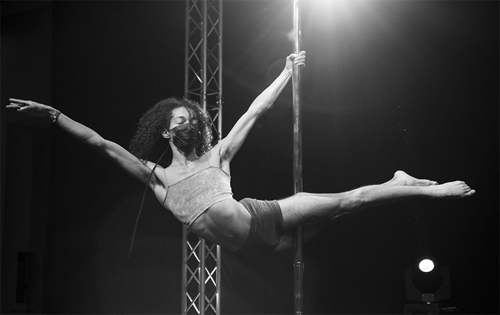 Pole dancer wearing mask executes a superman on stage.