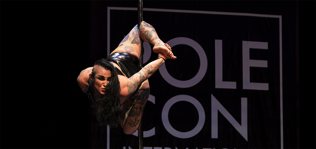Pole dancer demonstrates a gargoyle move on a pole.