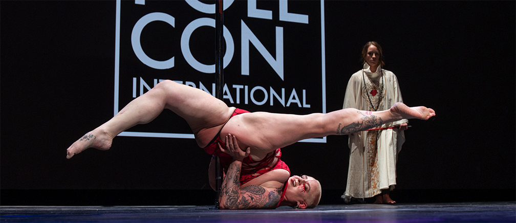 Tracy B performs at PoleCon 2024, doing a floor jade in front of the pole.